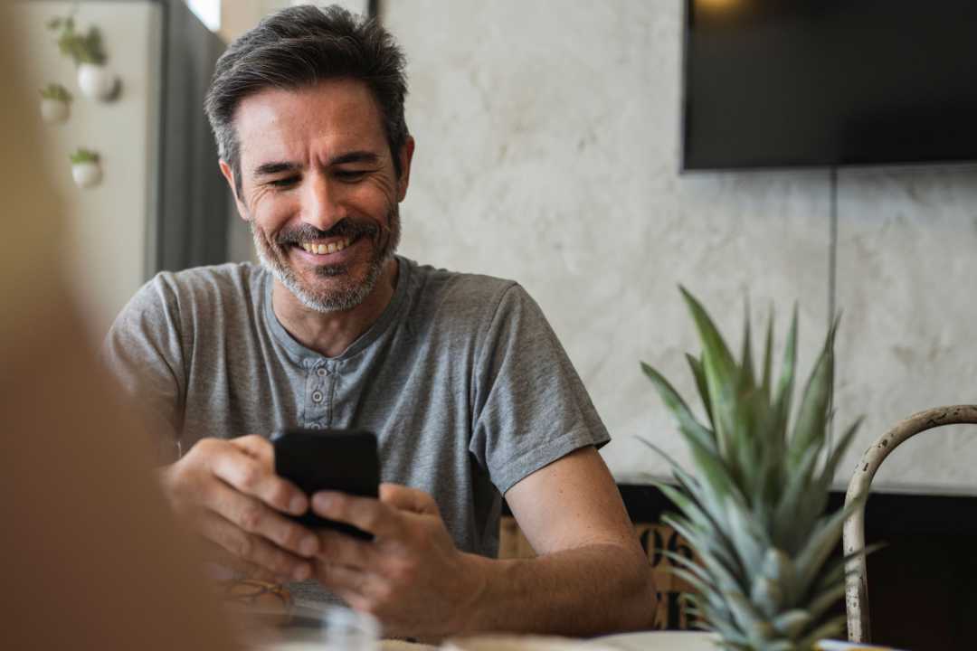 Mann am Smartphone im Café lächelt