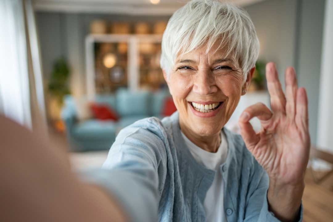 Zufriedene und lächelnde ältere Dame zeigt Handzeichen für perfekt